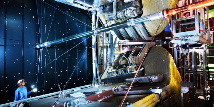 A man in a blue shirt and a safety helmet looking up at the Large Hadron Collider.